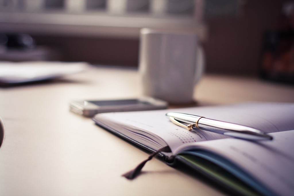 Cozy workspace with an open planner, pen, and coffee mug on a desk.